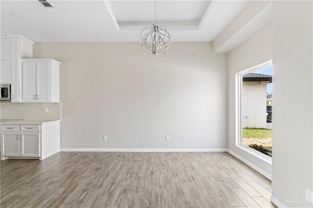 unfurnished dining area with a tray ceiling, light hardwood / wood-style flooring, and an inviting chandelier