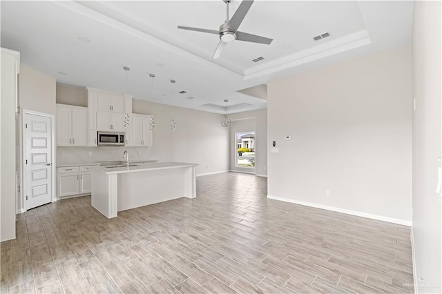 kitchen with a raised ceiling, white cabinetry, a kitchen island with sink, and light wood-type flooring