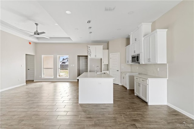 kitchen featuring ceiling fan, white cabinetry, a kitchen island with sink, and sink