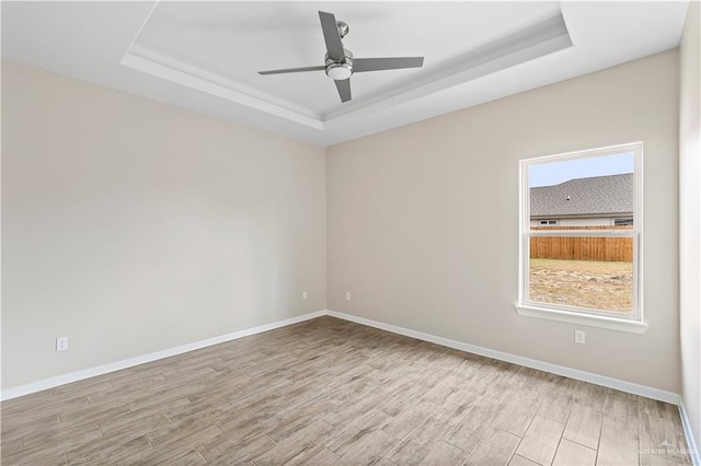 unfurnished room with light wood-type flooring, a raised ceiling, and a healthy amount of sunlight