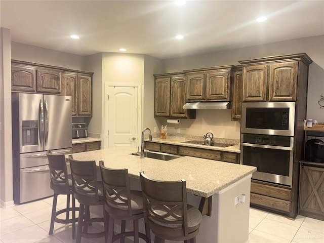 kitchen with dark brown cabinetry, sink, a breakfast bar, a center island with sink, and appliances with stainless steel finishes