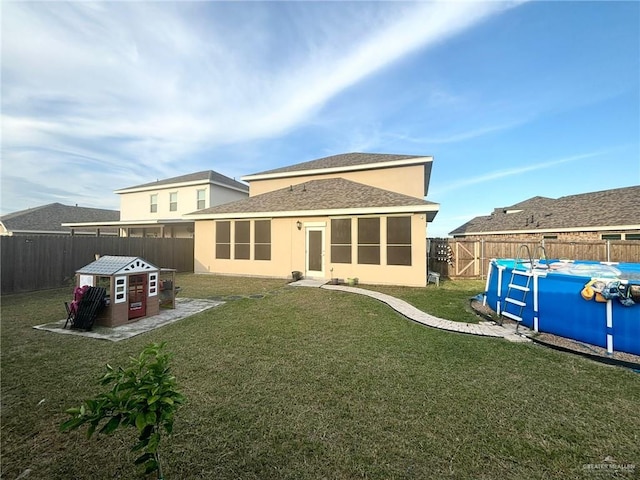 back of property with a fenced in pool and a lawn