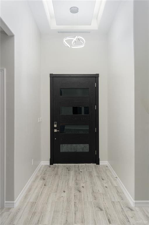 doorway with a raised ceiling, an inviting chandelier, and light hardwood / wood-style flooring