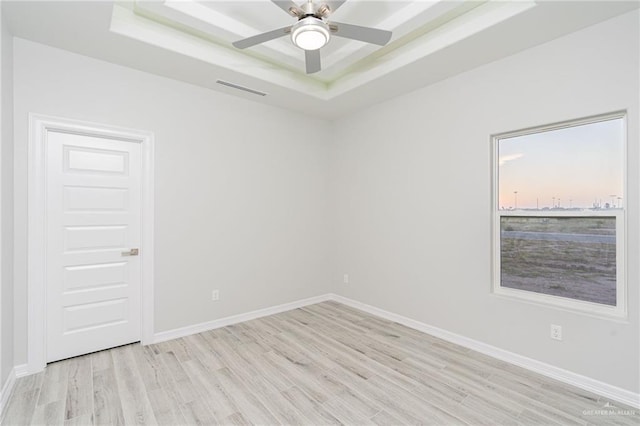 spare room with a tray ceiling, light hardwood / wood-style flooring, and ceiling fan