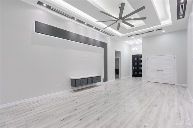 unfurnished living room featuring a tray ceiling, ceiling fan, a high ceiling, and light wood-type flooring