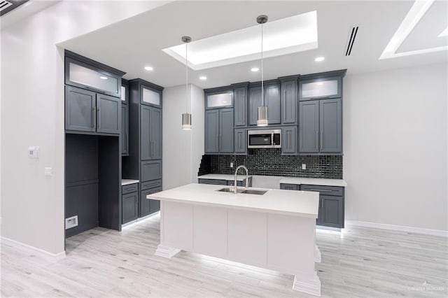 kitchen featuring sink, hanging light fixtures, backsplash, an island with sink, and a tray ceiling