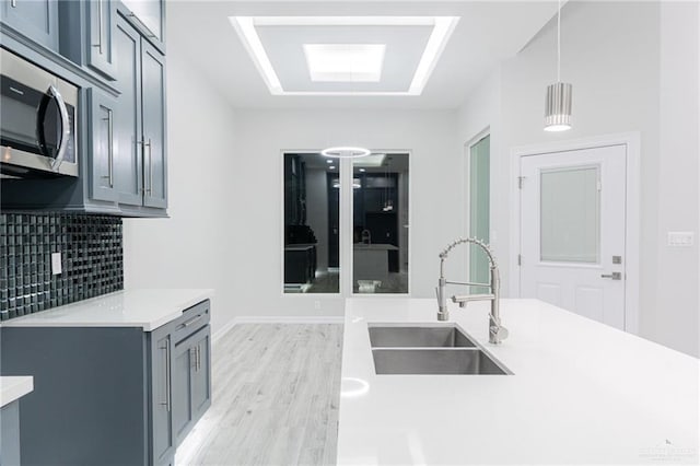 kitchen with pendant lighting, decorative backsplash, sink, and light hardwood / wood-style flooring