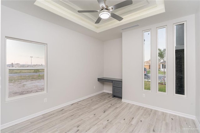 empty room featuring light wood-type flooring, a tray ceiling, and ceiling fan