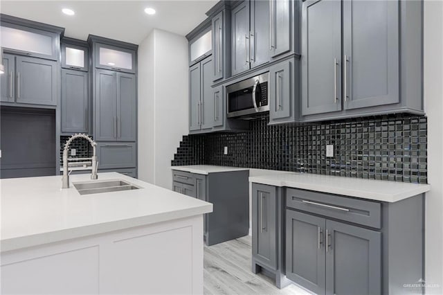 kitchen with backsplash, gray cabinetry, light wood-type flooring, and sink