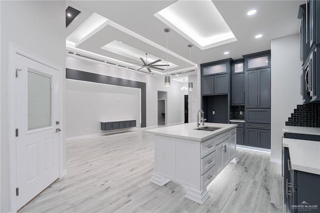 kitchen with decorative backsplash, ceiling fan, sink, pendant lighting, and a center island with sink