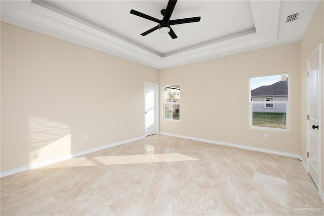 empty room featuring a tray ceiling, ceiling fan, and a healthy amount of sunlight