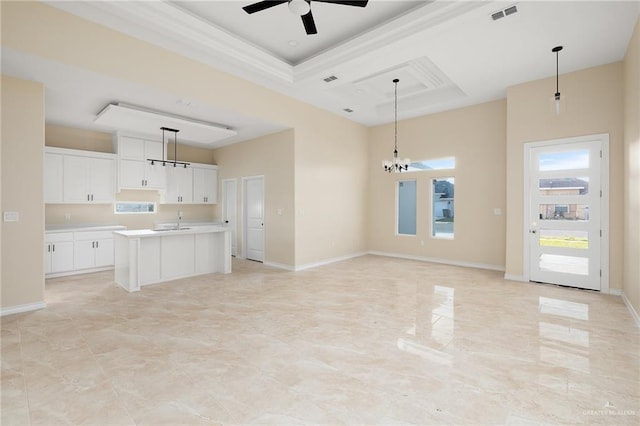 kitchen with a raised ceiling, decorative light fixtures, a kitchen island with sink, white cabinets, and ceiling fan with notable chandelier