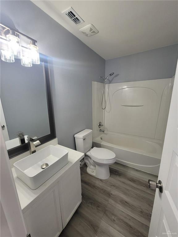 full bathroom with bathtub / shower combination, toilet, vaulted ceiling, vanity, and hardwood / wood-style flooring