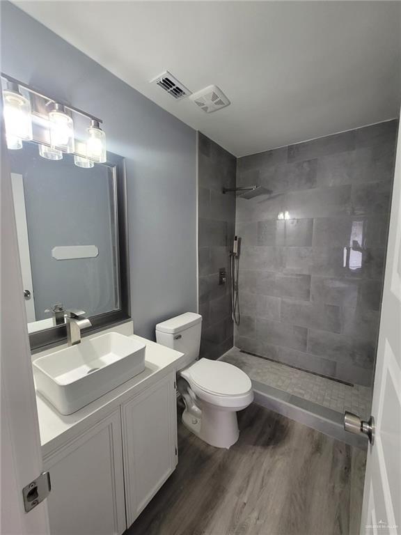 bathroom featuring tiled shower, wood-type flooring, toilet, and vanity