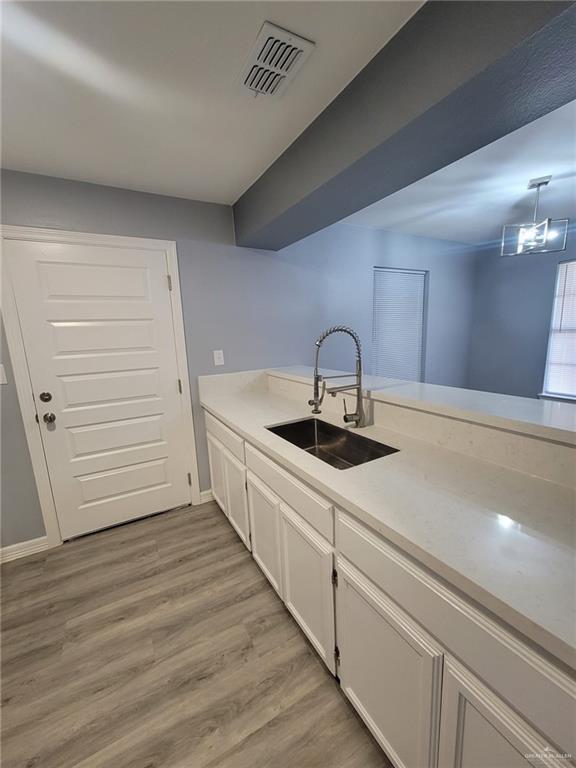 kitchen with sink, light hardwood / wood-style flooring, hanging light fixtures, and white cabinets