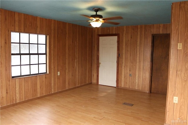 unfurnished room featuring ceiling fan, light hardwood / wood-style flooring, and wooden walls