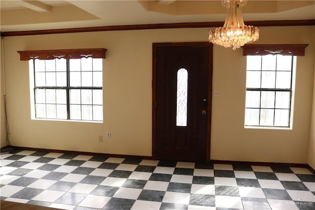 foyer with ornamental molding, a healthy amount of sunlight, a tray ceiling, and a notable chandelier