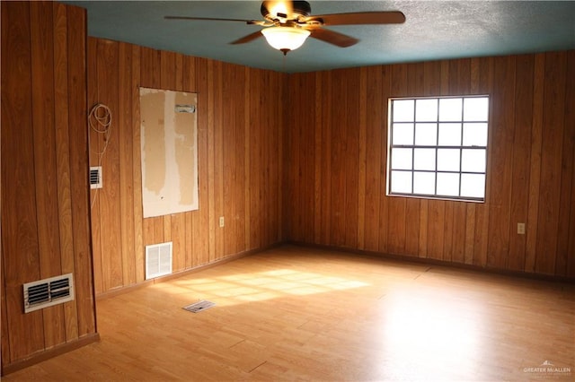 unfurnished room featuring a textured ceiling, ceiling fan, light hardwood / wood-style floors, and wood walls