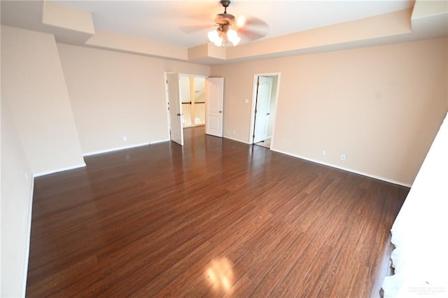 unfurnished room with ceiling fan, dark wood-type flooring, and a tray ceiling