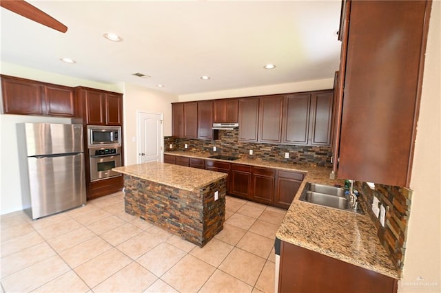 kitchen featuring sink, tasteful backsplash, light stone counters, a kitchen island, and appliances with stainless steel finishes