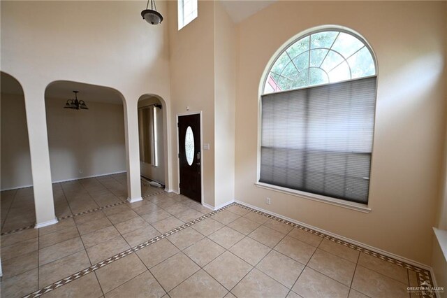 foyer featuring light tile patterned flooring, a towering ceiling, and a chandelier