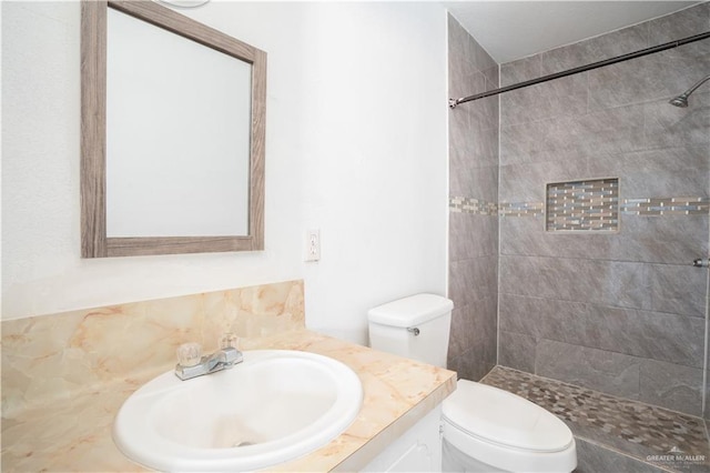 full bath featuring toilet, a tile shower, and vanity