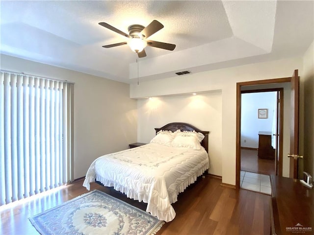 bedroom with ceiling fan, dark hardwood / wood-style floors, a raised ceiling, and a textured ceiling