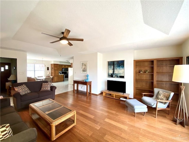 living room featuring a textured ceiling, light hardwood / wood-style floors, a raised ceiling, and ceiling fan