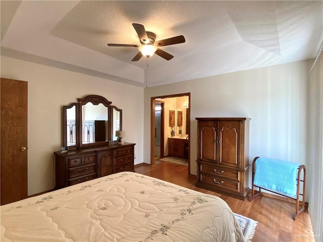 bedroom featuring dark wood-type flooring, a raised ceiling, a textured ceiling, and ensuite bathroom