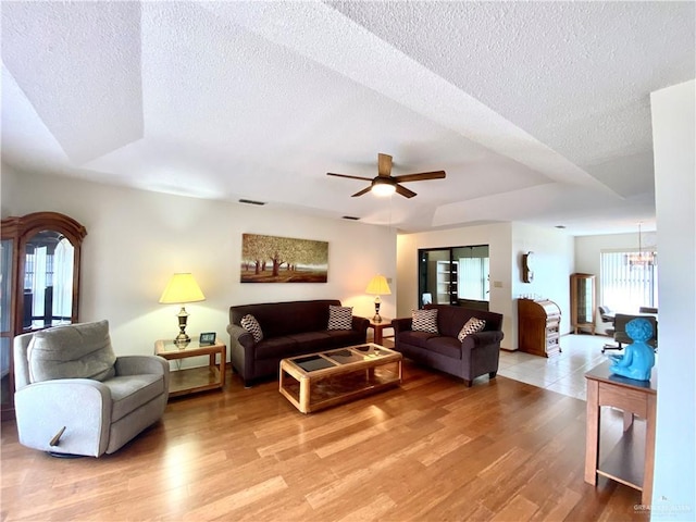 living room with ceiling fan with notable chandelier, a textured ceiling, and light wood-type flooring