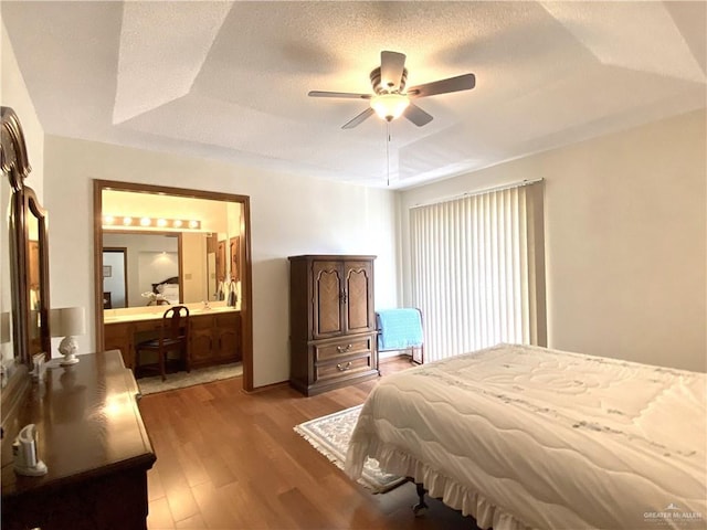 bedroom with hardwood / wood-style flooring, ceiling fan, ensuite bathroom, a tray ceiling, and a textured ceiling