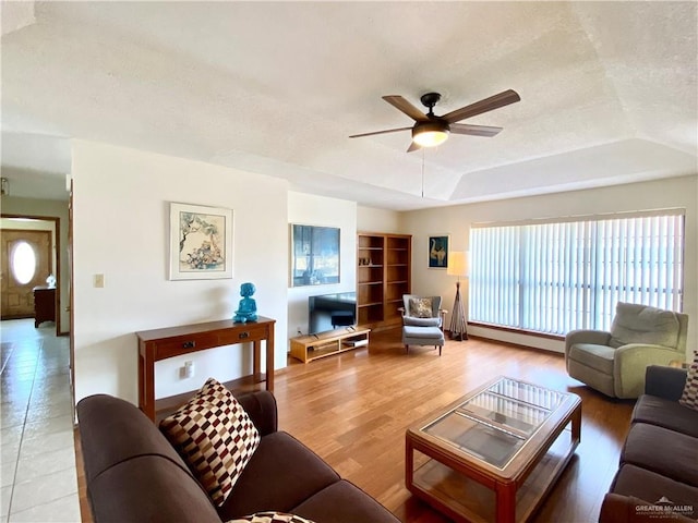 living room with a tray ceiling, plenty of natural light, ceiling fan, and light wood-type flooring