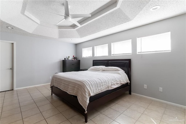 tiled bedroom with a tray ceiling, ceiling fan, and a textured ceiling