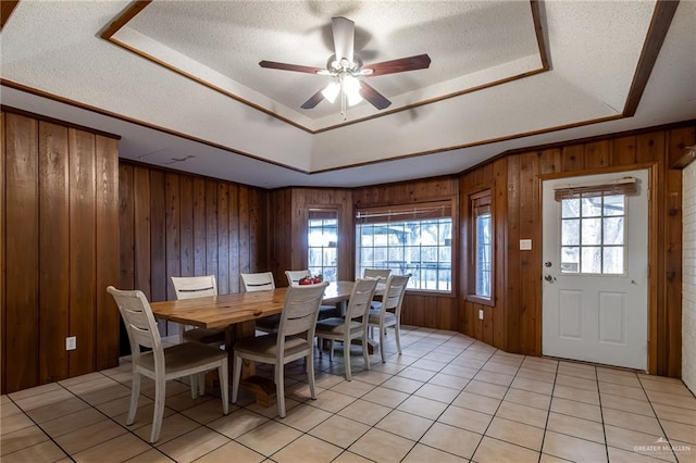 tiled dining area featuring ceiling fan, wood walls, a raised ceiling, and a textured ceiling