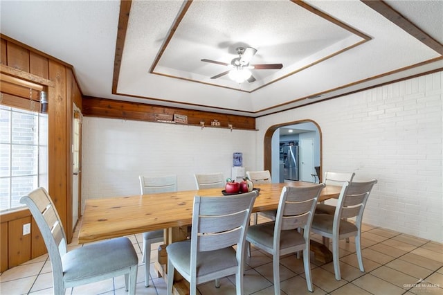 dining area featuring ceiling fan, light tile patterned floors, a textured ceiling, and brick wall