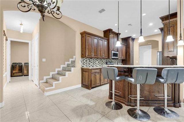 kitchen with decorative backsplash, kitchen peninsula, a kitchen breakfast bar, washer and clothes dryer, and pendant lighting