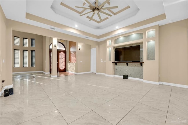 unfurnished living room featuring ceiling fan and a tray ceiling