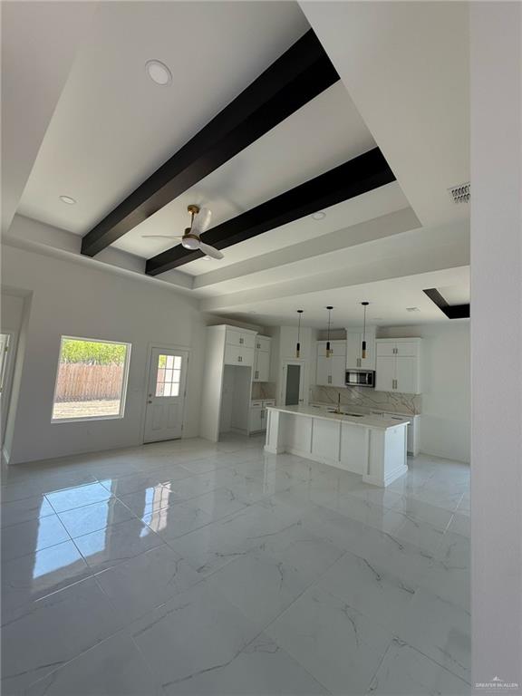 unfurnished living room with visible vents, beamed ceiling, marble finish floor, a raised ceiling, and a ceiling fan