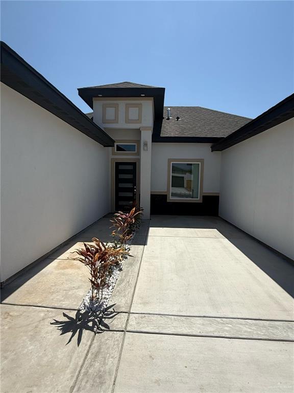 exterior space featuring a patio, concrete driveway, a shingled roof, and stucco siding