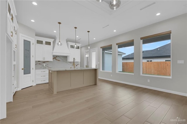 809 Azalea St, Mission, TX 78573 - kitchen featuring light wood-style flooring, decorative backsplash, glass insert cabinets, white cabinets, and an island with sink