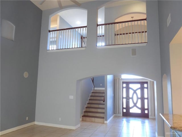 foyer with tile patterned flooring, stairway, baseboards, and a towering ceiling