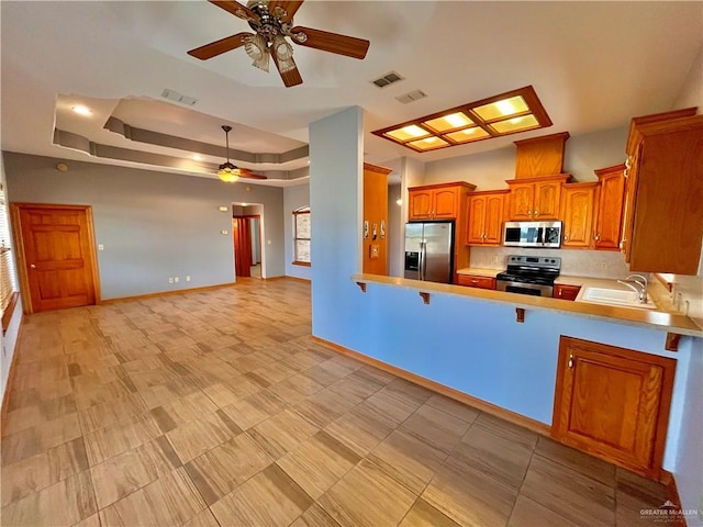 kitchen with kitchen peninsula, stainless steel appliances, a raised ceiling, ceiling fan, and sink