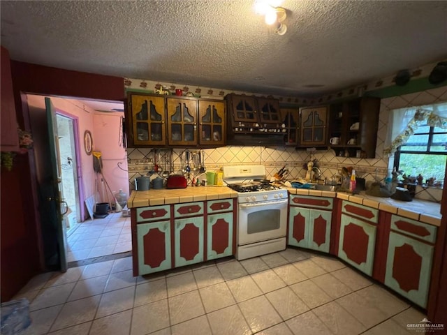 kitchen featuring white gas stove, decorative backsplash, tile counters, and light tile patterned floors