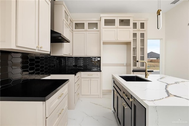 kitchen featuring light stone counters, sink, white cabinets, and hanging light fixtures