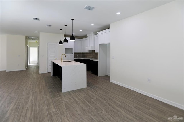 kitchen featuring decorative backsplash, sink, a center island with sink, white cabinets, and hardwood / wood-style floors