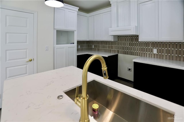 kitchen featuring white cabinets, tasteful backsplash, light stone countertops, and sink