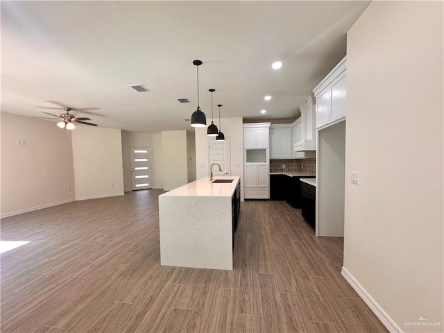 kitchen with backsplash, ceiling fan, an island with sink, white cabinetry, and wood-type flooring