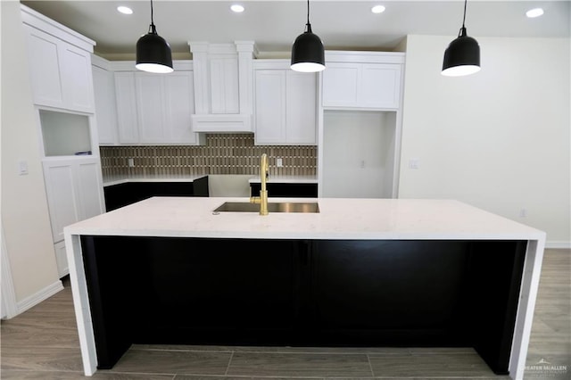 kitchen featuring white cabinetry, a center island with sink, decorative light fixtures, and sink