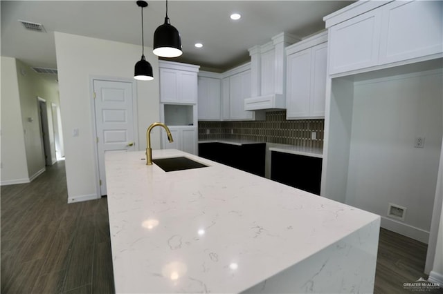 kitchen featuring tasteful backsplash, light stone counters, sink, decorative light fixtures, and white cabinetry