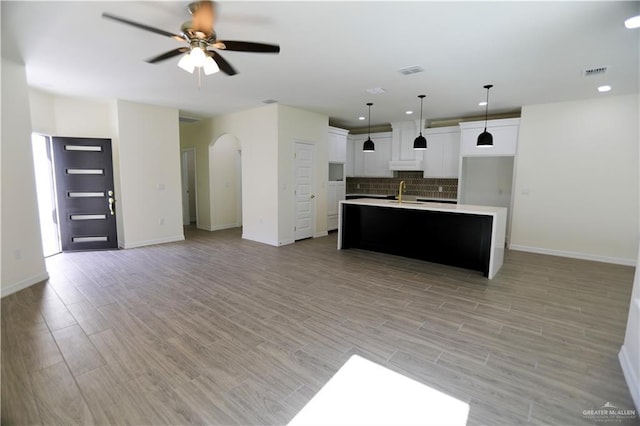 kitchen featuring ceiling fan, backsplash, an island with sink, pendant lighting, and white cabinets